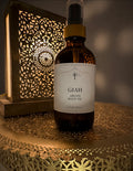 A bottle of GIAH Argan Body Oil stands on a decorative brass tray with a warm, glowing cutout lantern in the background.